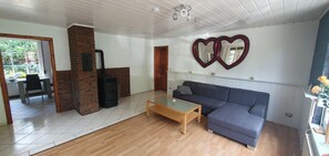 A living room with a wooden floor, a blue sofa, a glass coffee table, and a brick fireplace. - Herzkate Vacation Rental (Bremervörde)