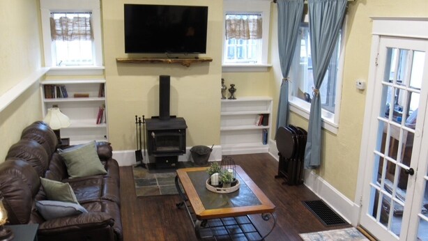 Una sala de estar acogedora con chimenea, televisor montado en la pared y un rincón de descanso con sofá y mesa de centro.