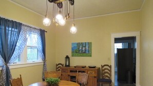 Un comedor con una mesa y sillas de madera, una araña y un cuadro en la pared.