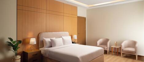 A modern bedroom with a large bed, bedside tables, a nightstand, two chairs, and a small table with a lamp.