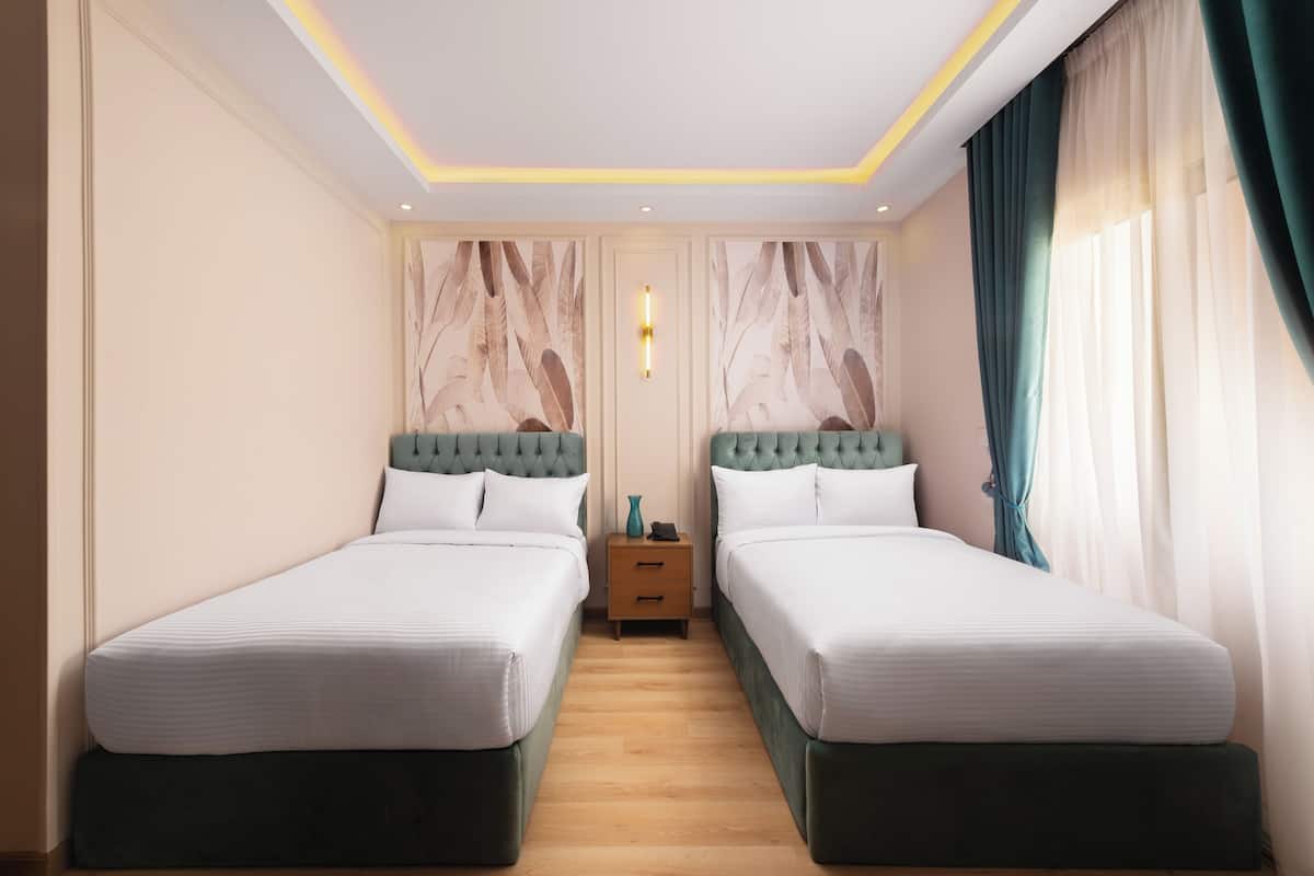 A hotel room with two single beds, a nightstand, and a wall-mounted light fixture.