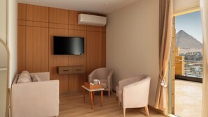 Hotelkamer met een wand van houten panelen, een flatscreen televisie, een bank, een stoel, een klein tafeltje met dienblad en uitzicht op een piramide door het raam.