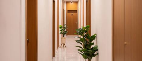 Un pasillo de hotel con puertas de madera, suelo de mármol y plantas en macetas.