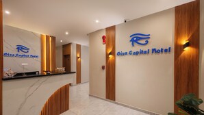 Een receptie met een marmeren balie, houten details en een bord met de tekst Oiza Capital Hotel.