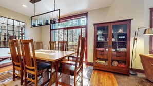 A dining area with a wooden table and chairs, a large window with a view of trees, and a wooden cabinet with glass doors.