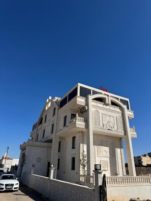 A multi-story building with a prominent entrance featuring intricate carvings and a clock. - Lalişa Otel (Midyat)