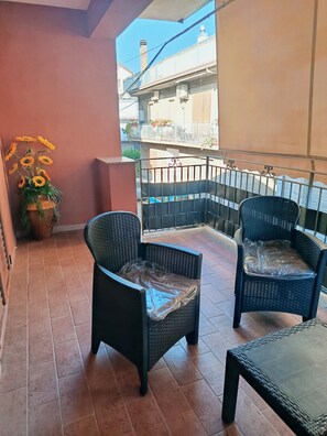 Un balcon avec deux fauteuils en osier, un pot de fleurs aux fleurs jaunes et un sol carrelé.