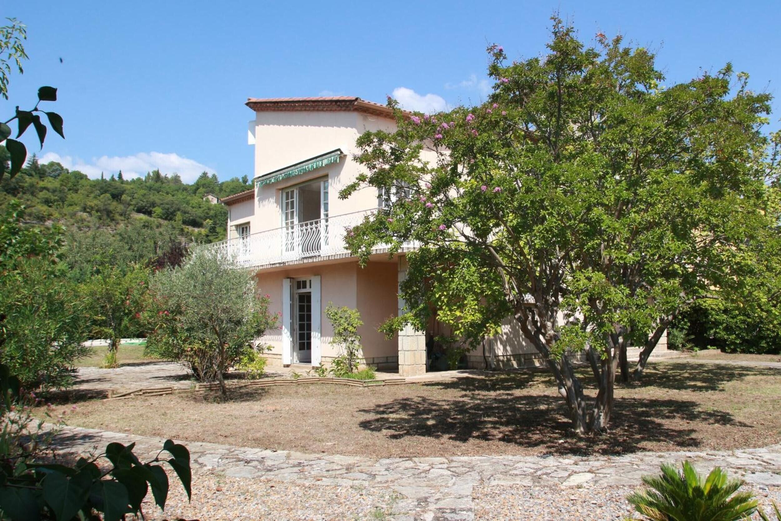 Un edificio a due piani con un balcone, immerso nel verde e con un vialetto in pietra.