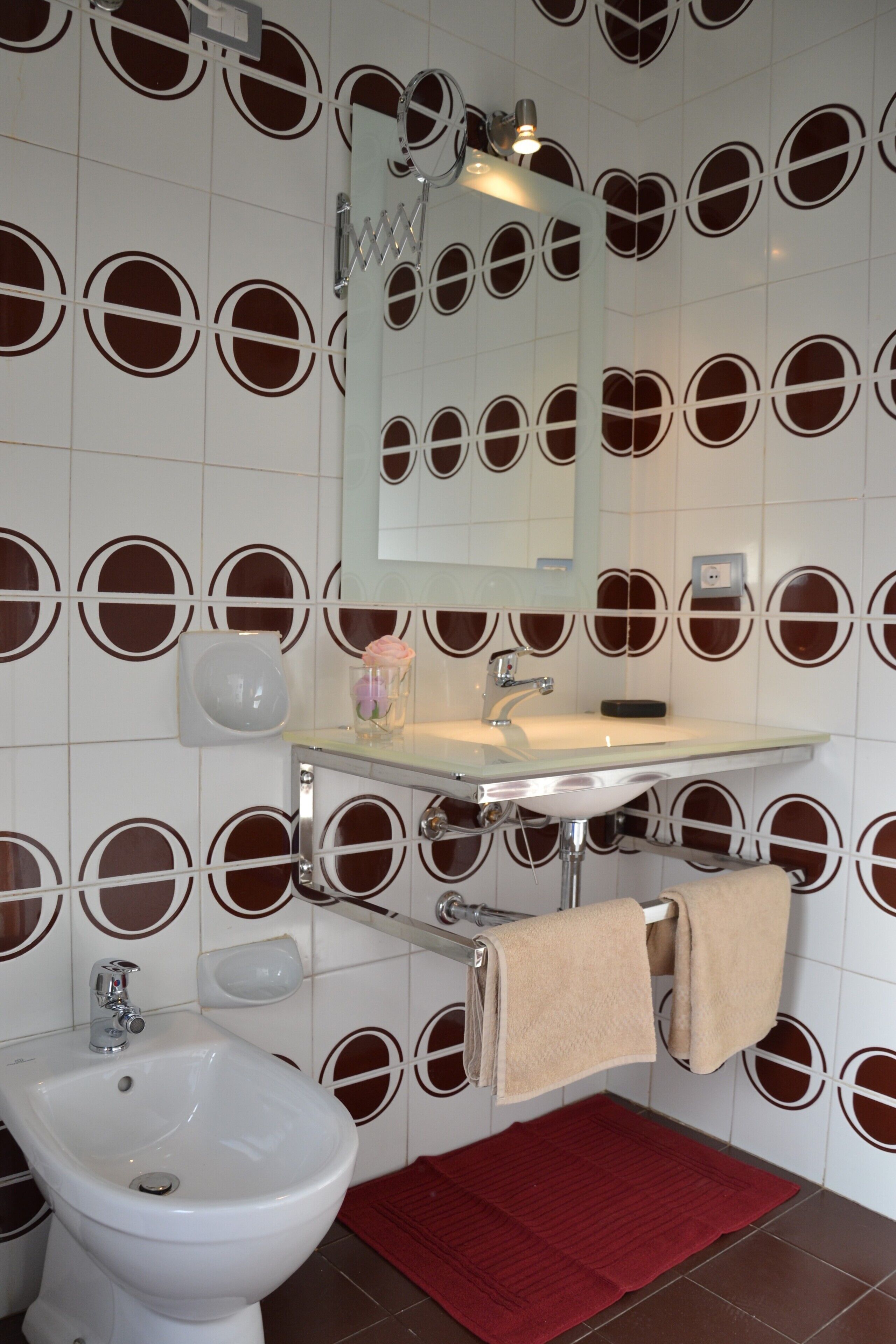 A bathroom with a bidet, sink, mirror, and patterned wall tiles.