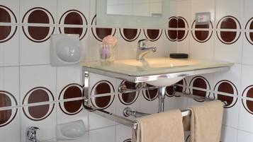 A bathroom with a bidet, sink, mirror, and patterned wall tiles.