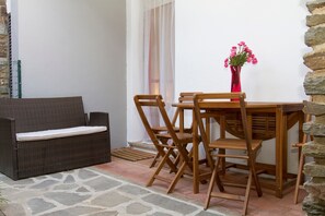 A patio with a wicker sofa, wooden chairs, a table, and a vase with flowers. - Holiday Home 'Cala Lupo' with Private Terrace, Private Garden and Air Conditioning (Stintino)