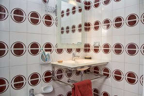 A bathroom with a white sink, mirror, and red circular wall tiles.
