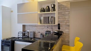 Cocina compacta con horno integrado, cafetera y microondas sobre una estantería.
