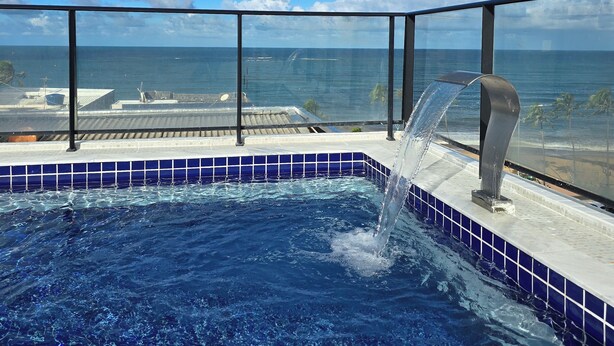 Una piscina con fuente de agua, vista despejada al océano y borde revestido de azulejos azules.