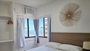 Habitación de hotel con cama, ventana con vista a la playa, ventilador de techo y un adorno colgado en la pared.