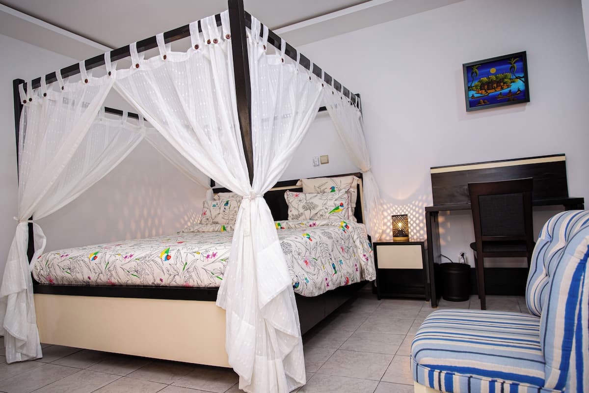 A bedroom with a four-poster bed, a nightstand, a chair, and a wall-mounted painting.