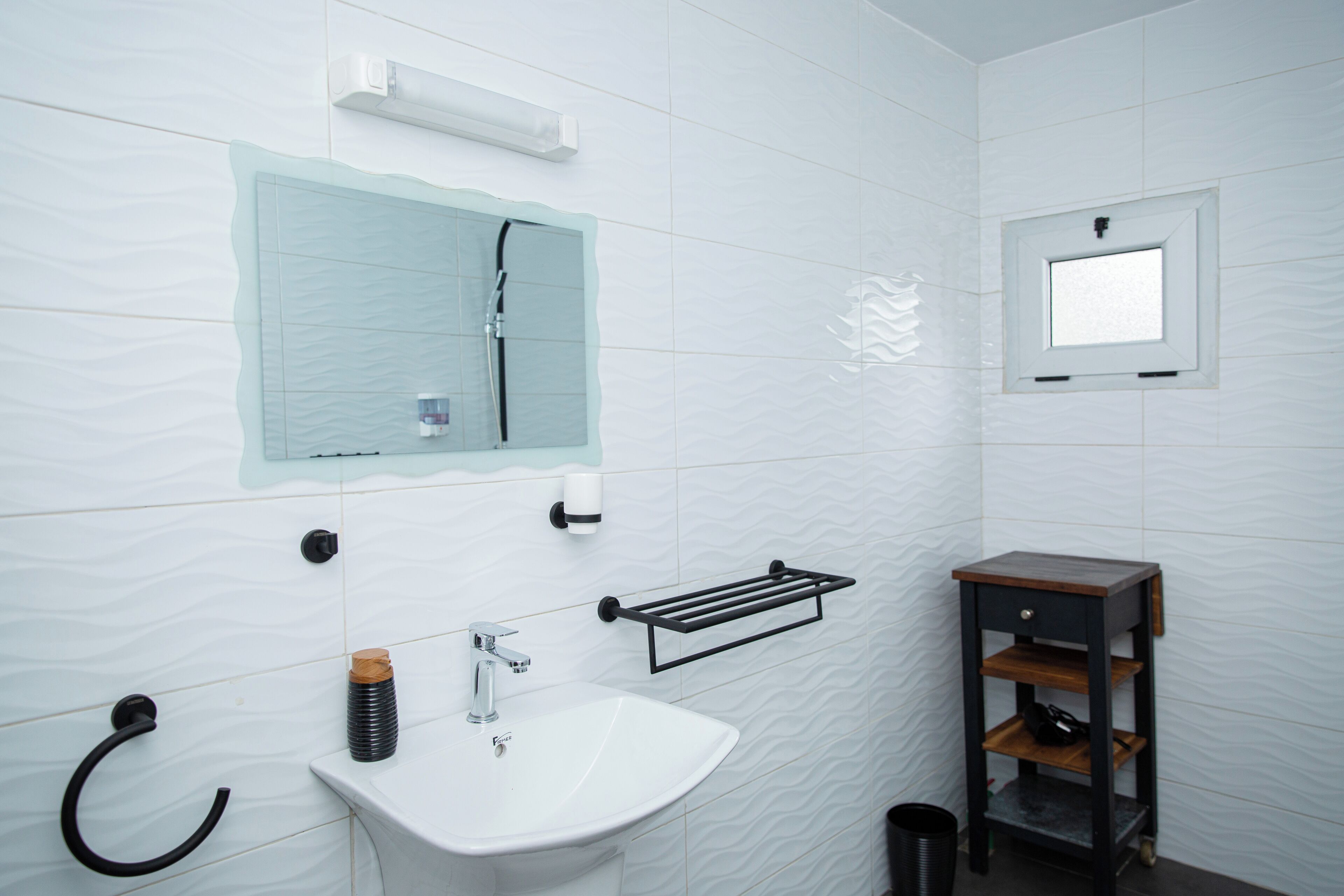 A bathroom with a white sink, a mirror, a towel rack, and a small wooden cabinet.