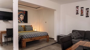 Un dormitorio moderno con una cama de madera, un escritorio con una silla, un sofá y un televisor montado en la pared.