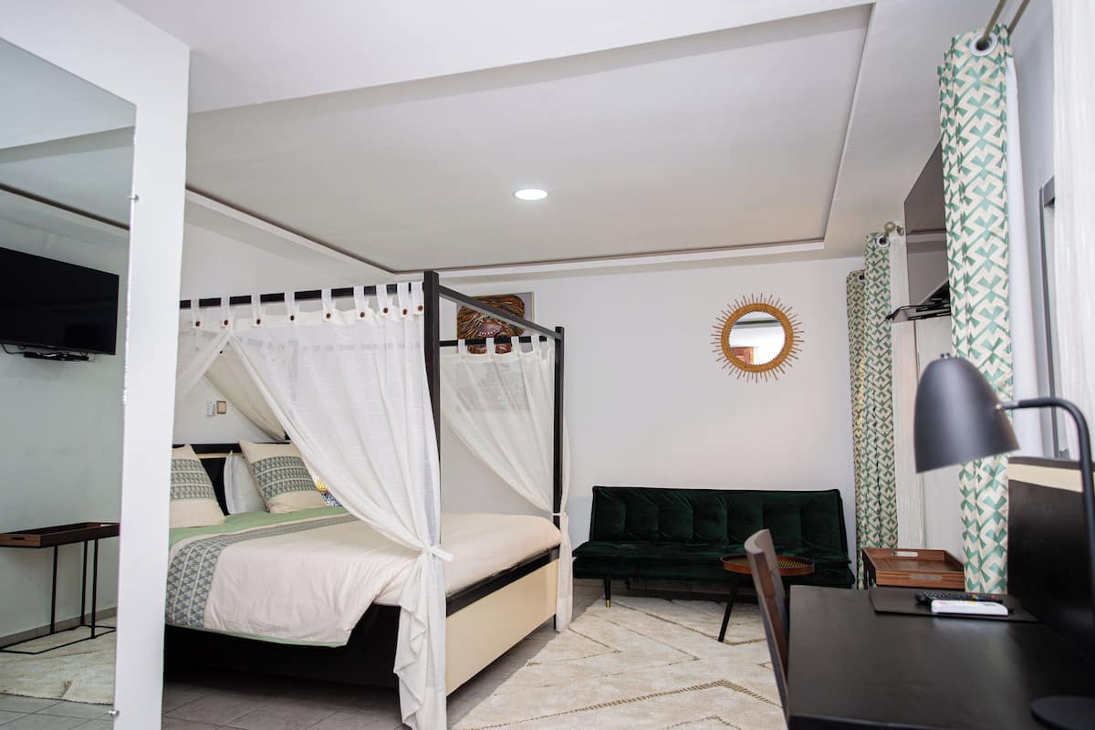 A bedroom with a bed, bedside table, desk, chair, and a mirror on the wall.
