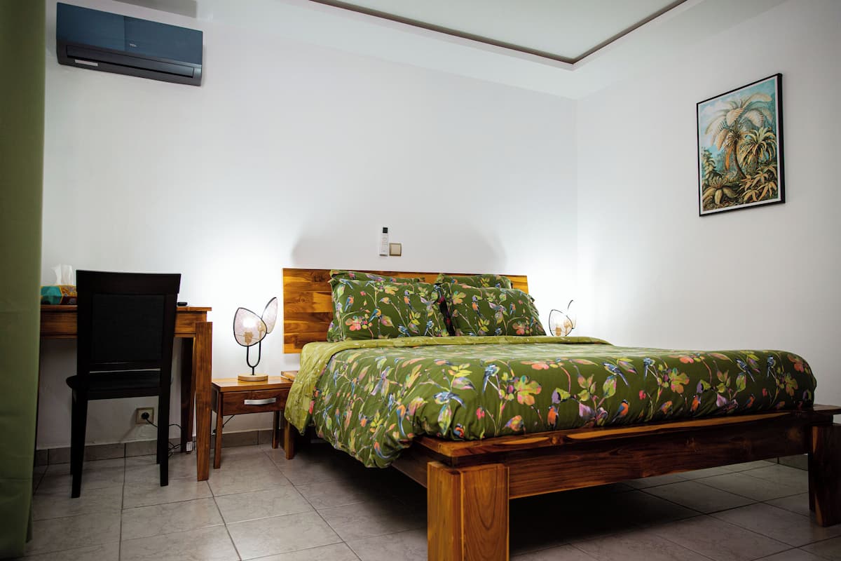 A bedroom with a wooden bed, a desk, a chair, and a nightstand with a lamp.