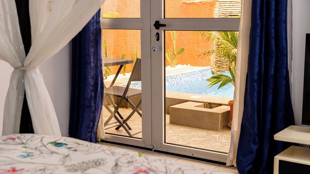 Un dormitorio con cama, una silla y un ventanal corredera que da a una zona de piscina.