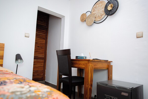 A hotel room with a wooden door, a dining table with chairs, a refrigerator, and wall decor. - Villa Jaddis (Abidjan)
