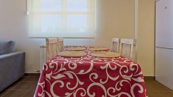 Une table à manger recouverte d’une nappe à motifs rouges et blancs, quatre sets de table en tissu, et une fenêtre donnant sur des immeubles.