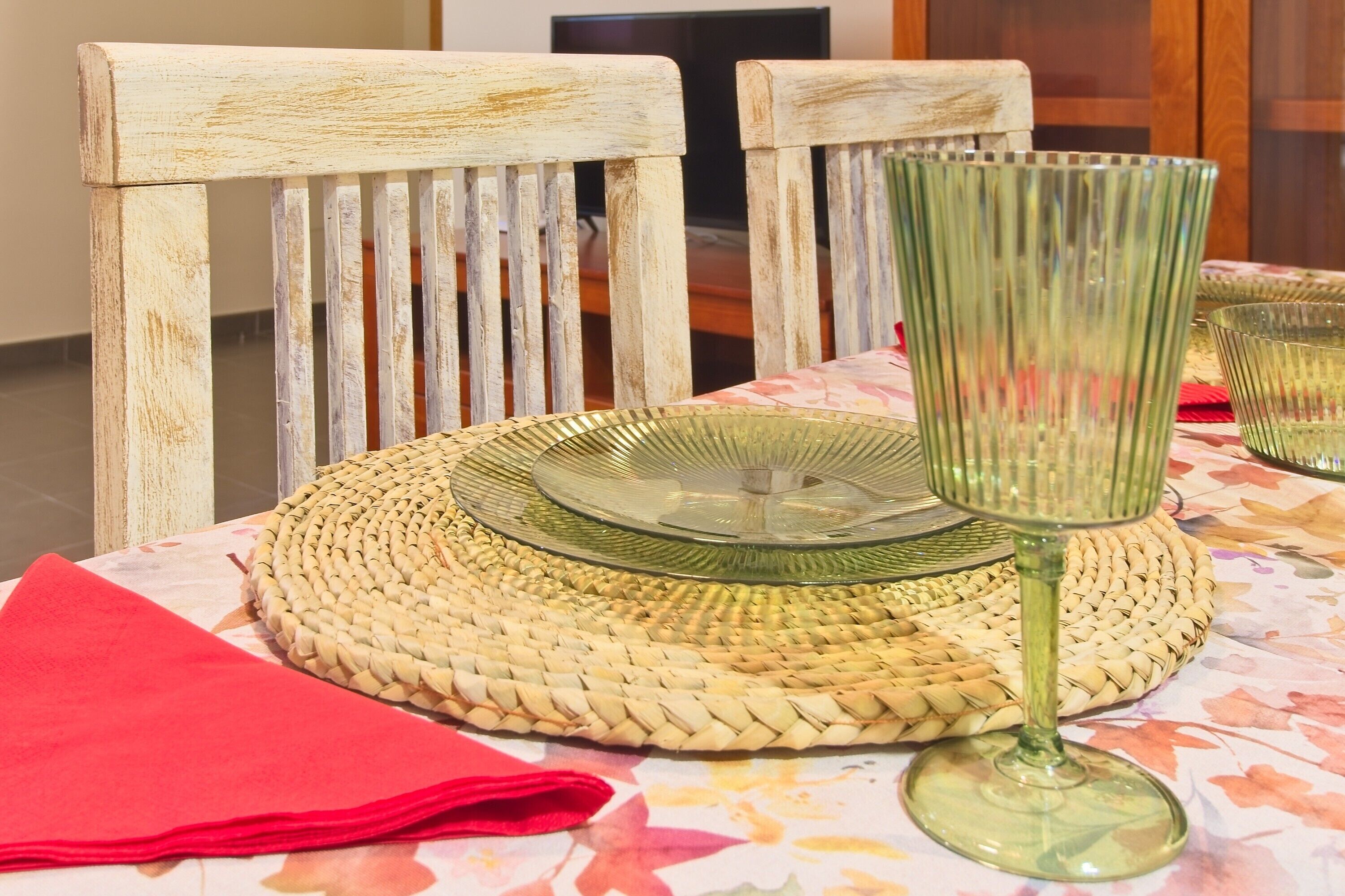 Una mesa con un posavasos tejido, un plato de vidrio, una copa de tallo y una servilleta roja.
