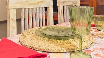 A table set with a woven placemat, a glass plate, a glass stemware, and a red napkin.