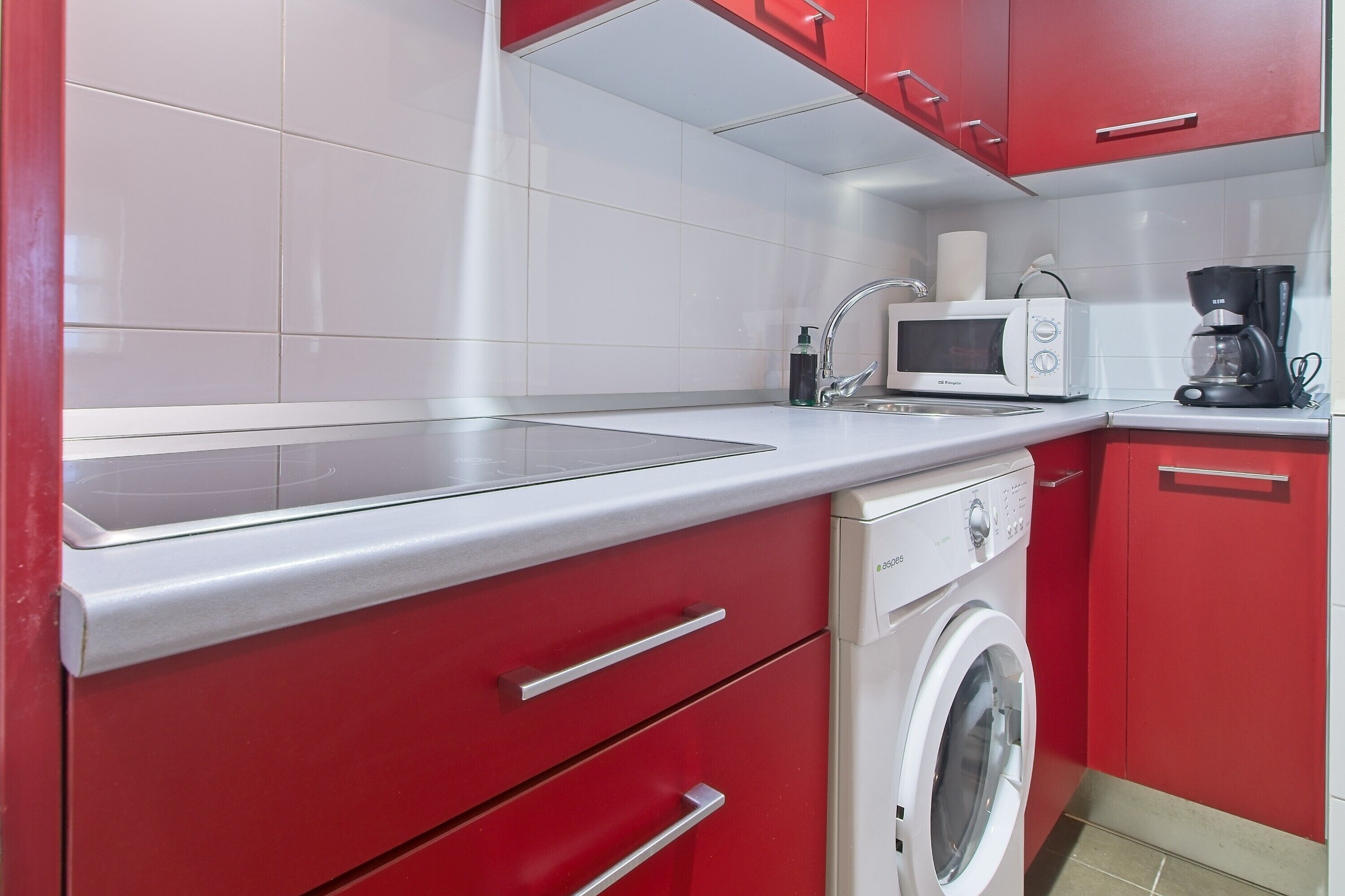 Een keuken met een magnetron, koffiezetapparaat en wasmachine.