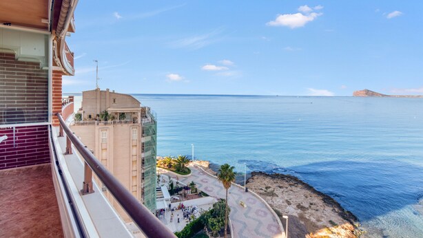 Un balcon donnant sur la mer, un immeuble à la façade en briques et un ciel dégagé.