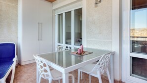 Un coin repas avec une table en verre, des chaises blanches, une chaise bleue et un meuble blanc.