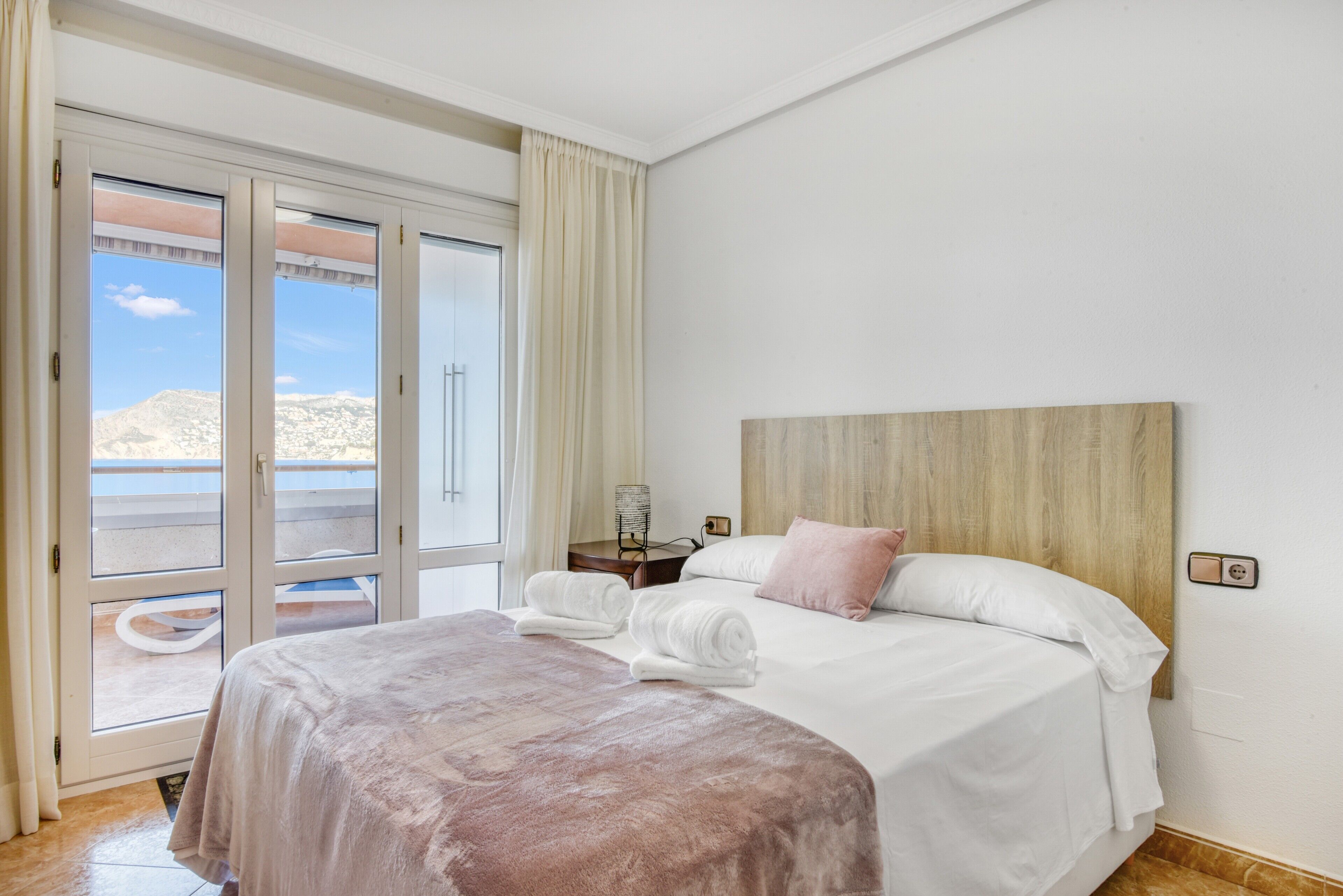 Une chambre d’hôtel avec un lit, une tête de lit, une table de chevet et une vue sur l’extérieur, accessible par une porte coulissante.