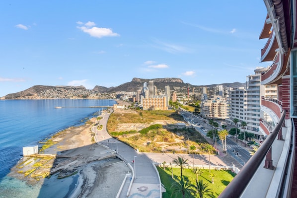 A coastal cityscape with a beach, urban buildings, and a mountainous backdrop.