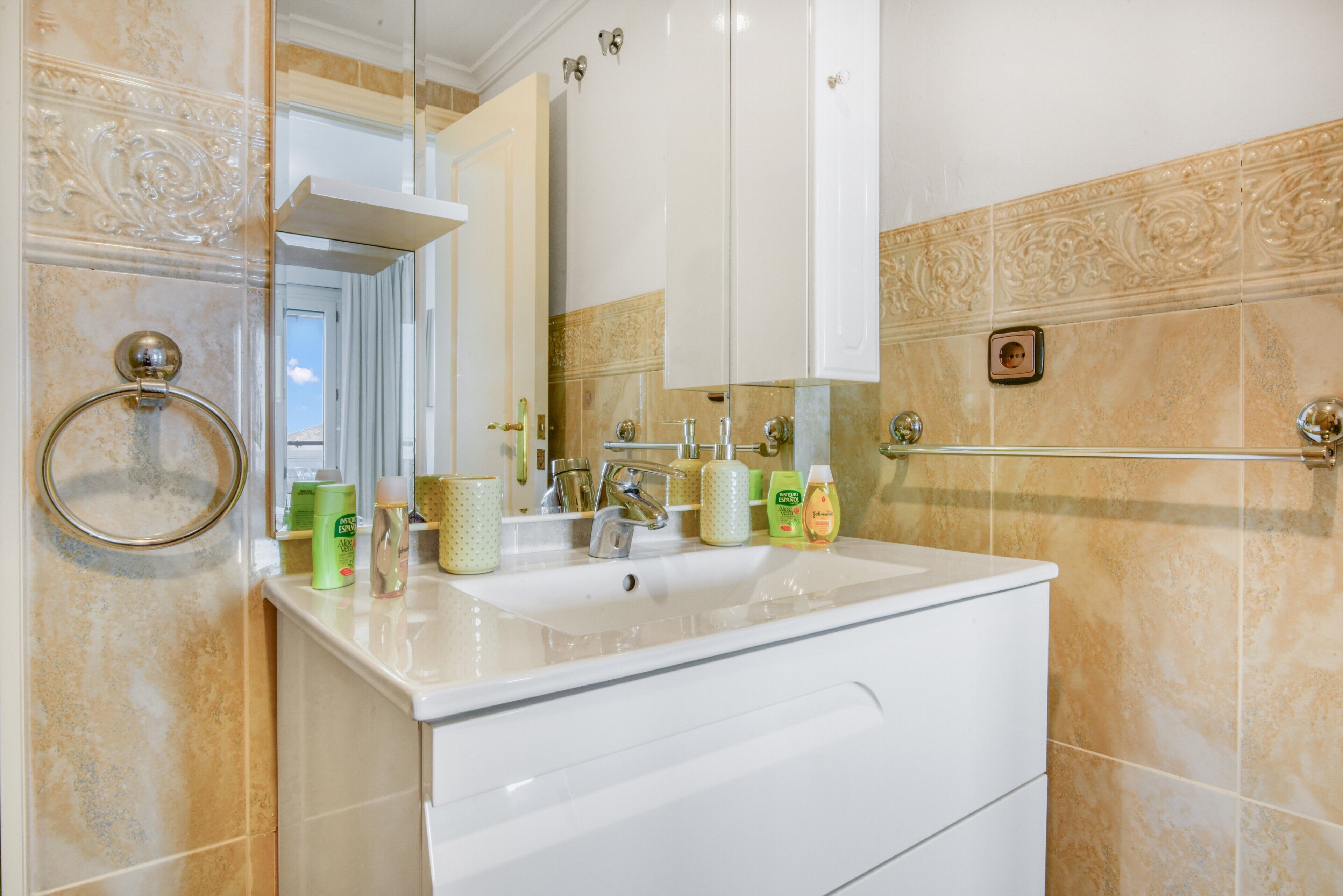 Une salle de bain équipée d’un lavabo, d’un miroir, d’un porte-serviettes et d’articles de toilette.