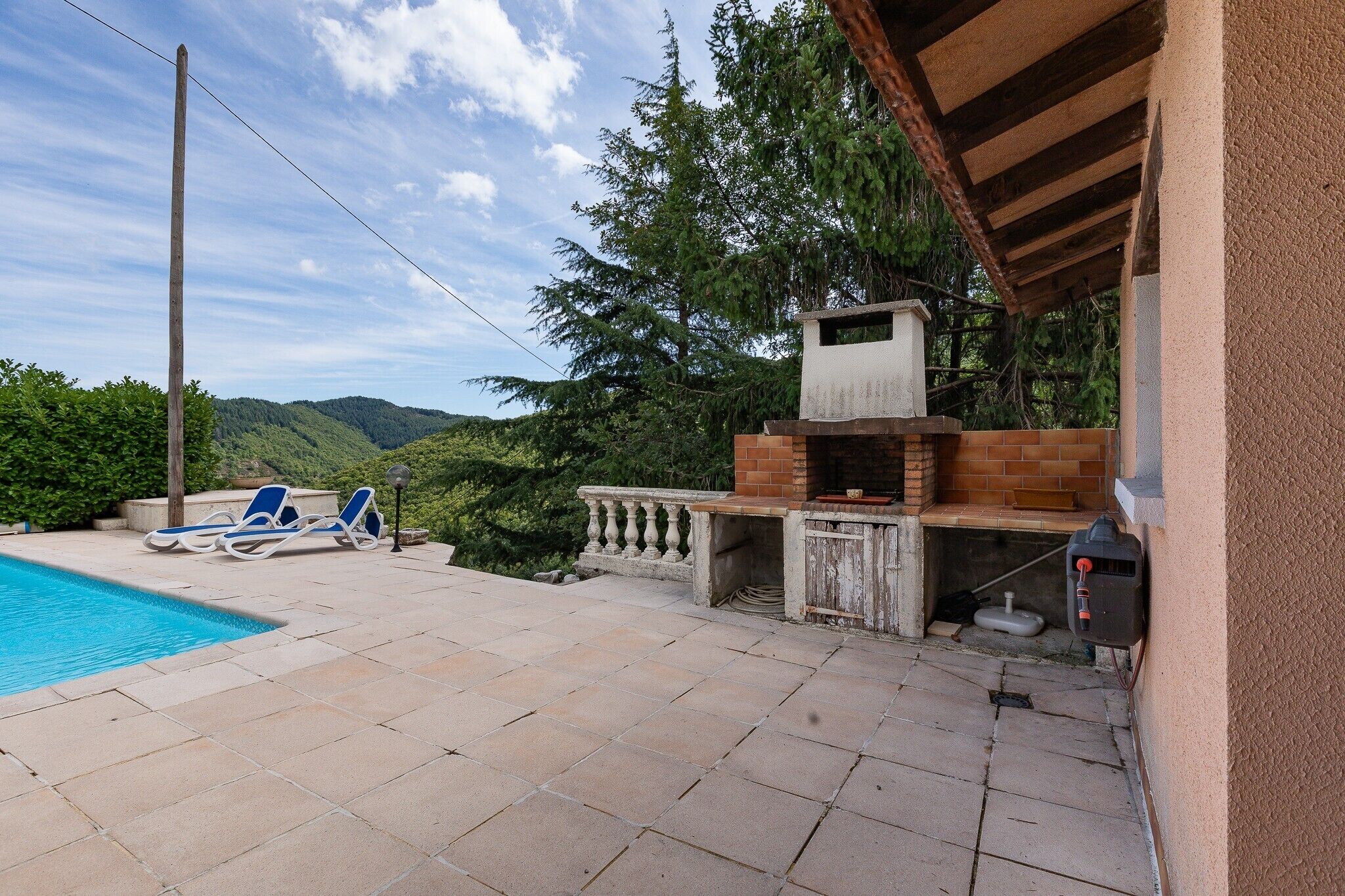 Ein Poolbereich mit Liegestühlen, einem Grill und Blick auf die Berge.