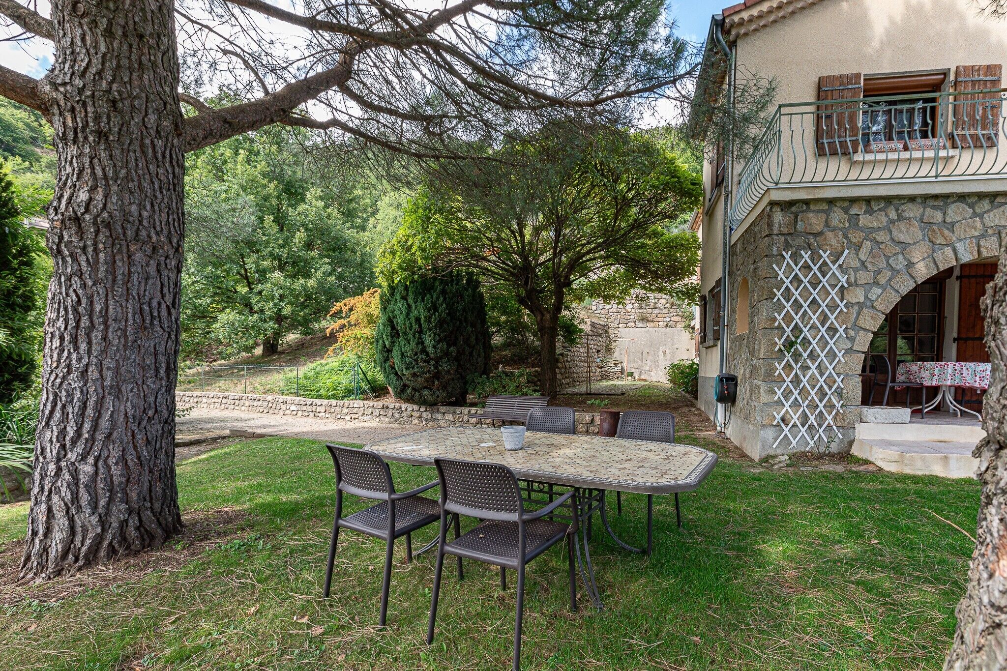 Une terrasse avec une table et des chaises, entourée d’arbres et d’un mur de pierre.