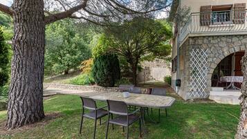 A patio with a table and chairs, surrounded by trees and a stone wall.