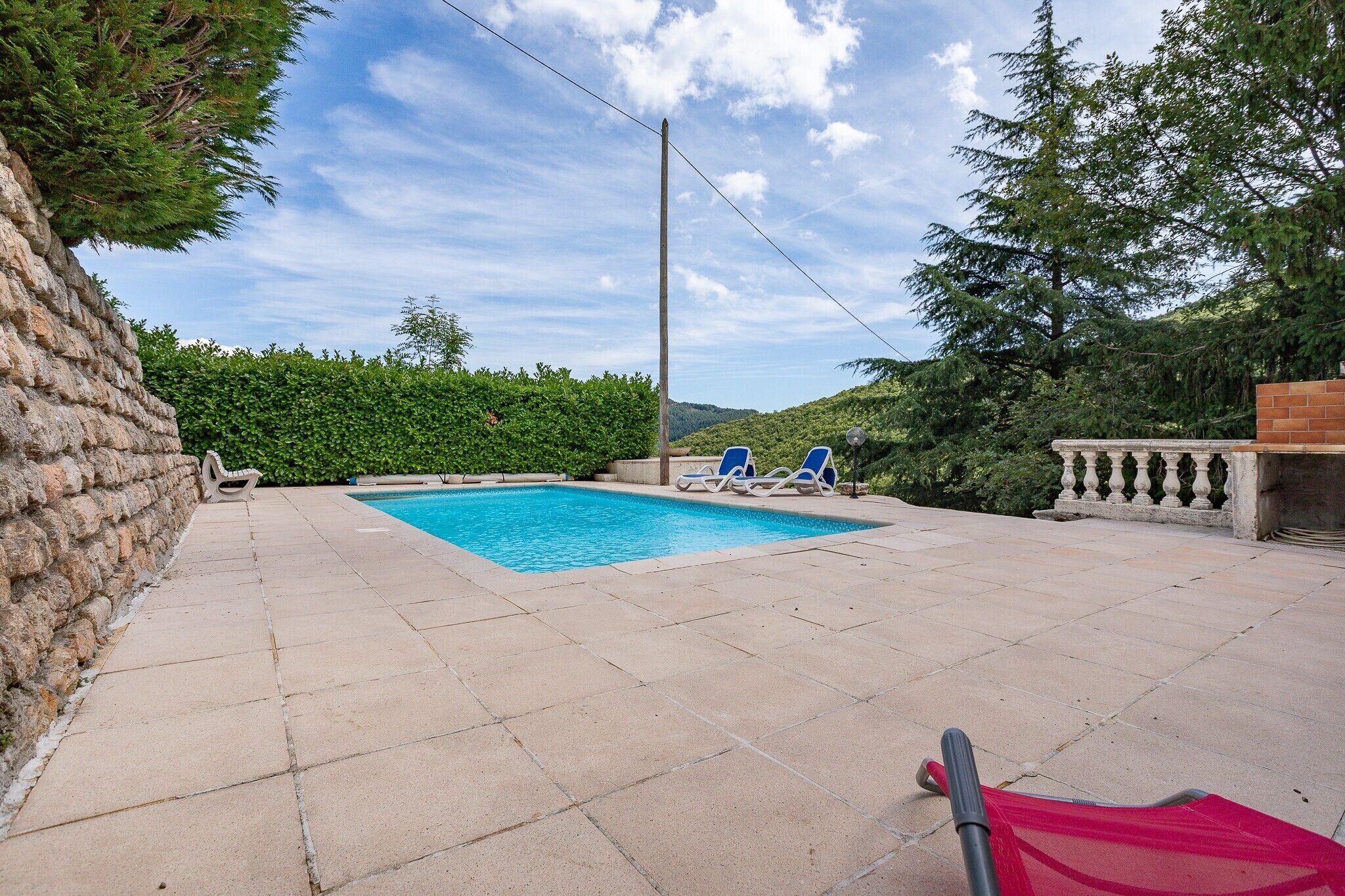 Une piscine avec des chaises longues, un mur en pierre et une haie.