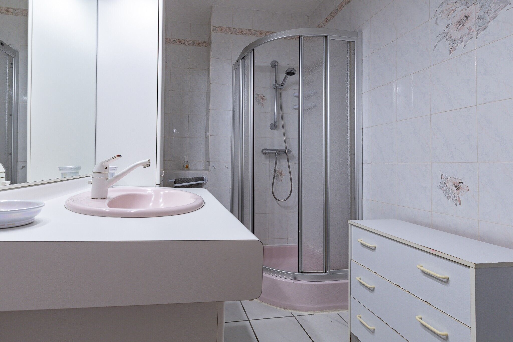 A bathroom with a white sink, a glass shower enclosure, and a white cabinet with drawers.
