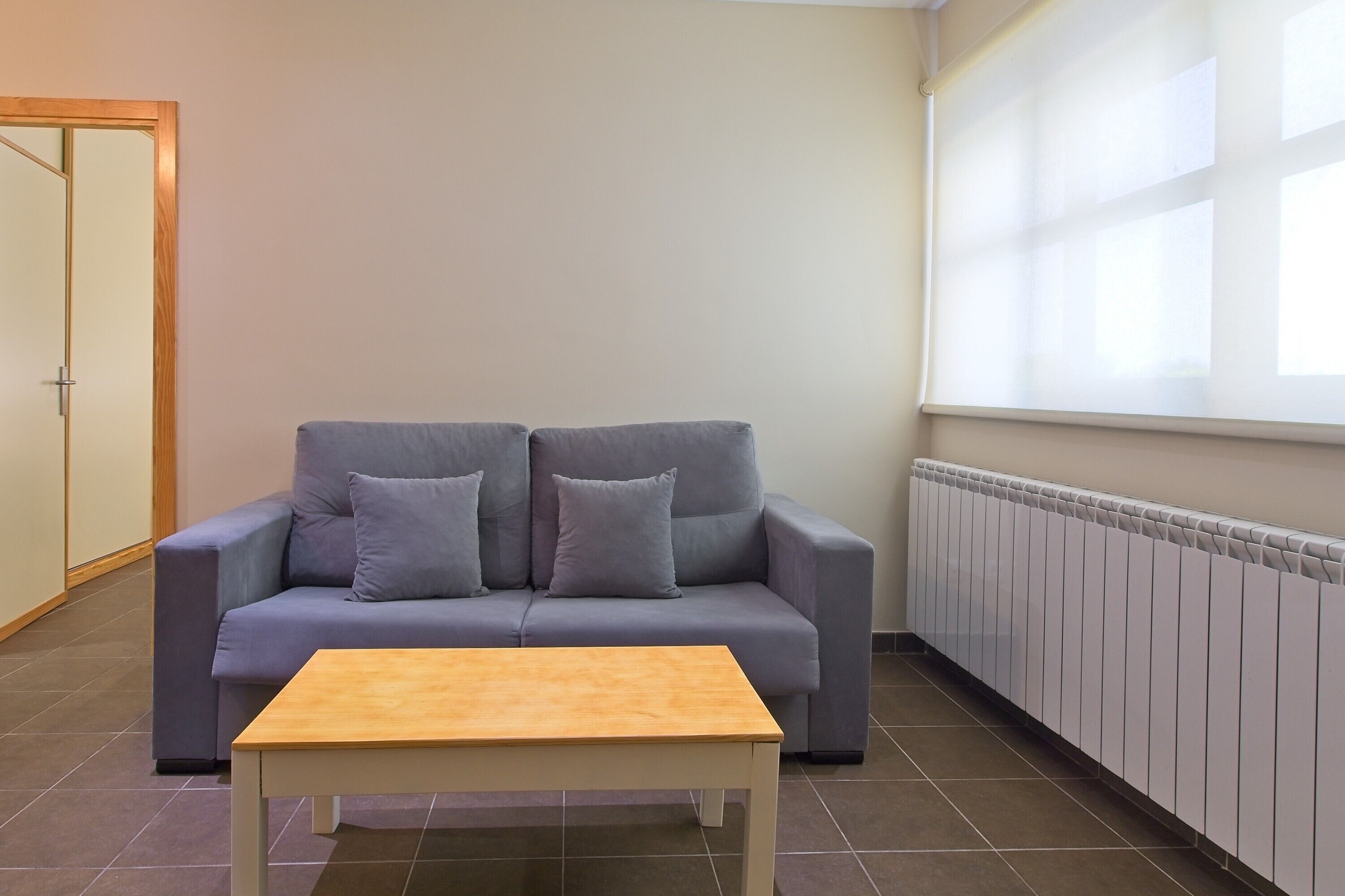 Una habitación con un sofá gris, una mesa de madera, un radiador y una puerta.