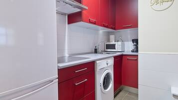 Eine moderne Küche mit roten Schränken, einem weißen Kühlschrank, einer Waschmaschine, einer Mikrowelle und einer Kaffeemaschine.