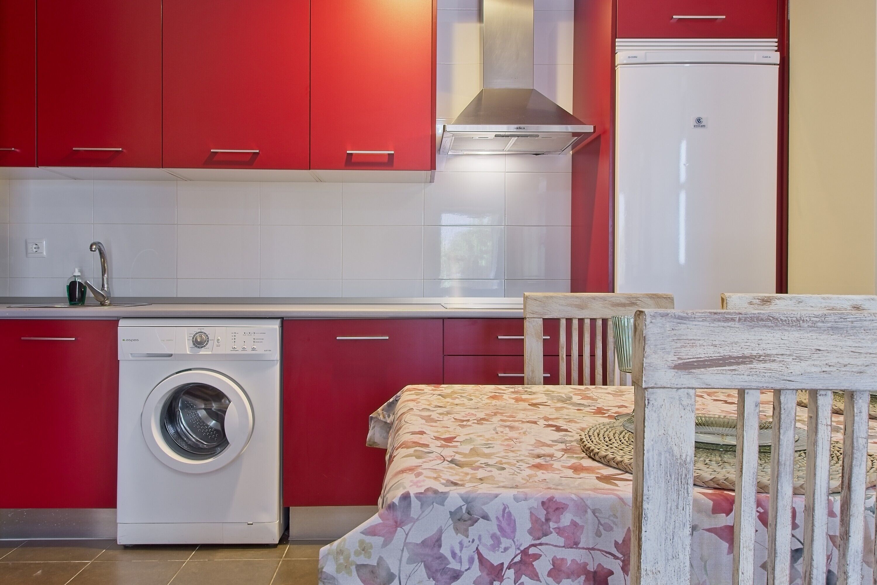Une cuisine compacte équipée d’un lave-linge, d’un réfrigérateur et d’un lit recouvert d’une courtepointe à motifs floraux.