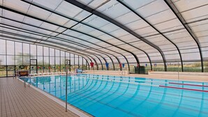 Una piscina interior con techo curvo, paredes de vidrio transparente y suelo de baldosas.