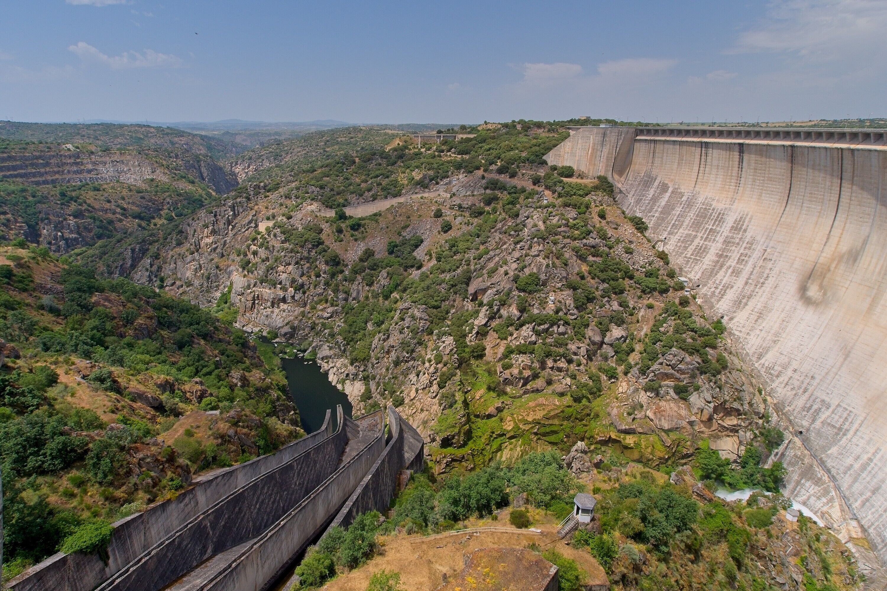 Un grand barrage, avec un terrain escarpé et rocheux, et une rivière en contrebas.