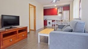 A living room with a TV, a sofa, a coffee table, and a kitchen in the background.