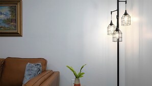 Ett vardagsrum med en brun soffa, ett litet runt bord med en växt och en fjärrkontroll, och en golvlampa med tre ljuskällor.