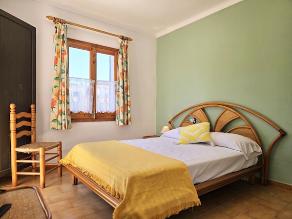 A bedroom with a wooden bed, a chair, a window with floral curtains, and a green wall.