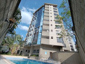 A high-rise building with a swimming pool, surrounded by greenery and trees.