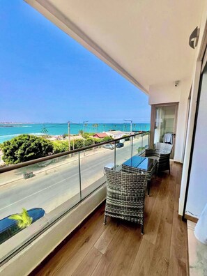 A balcony with wicker furniture, a glass table, and a view of the ocean and street. - Luxurious Apt - Sea View (El Mansouria)